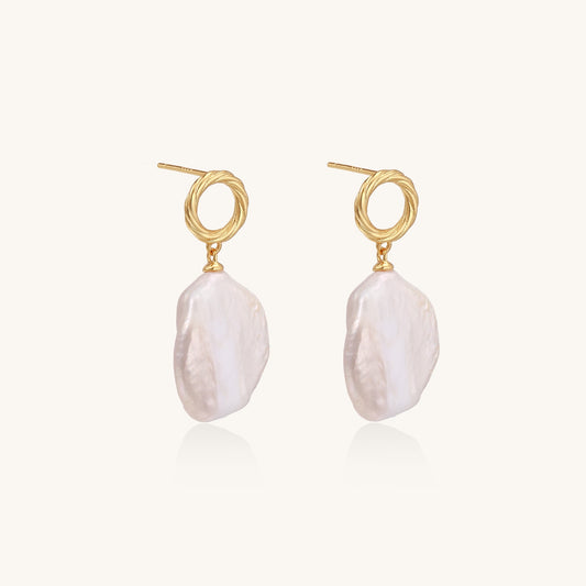 Gold-plated twisted stud earrings with large blush baroque pearls hanging elegantly on white background.