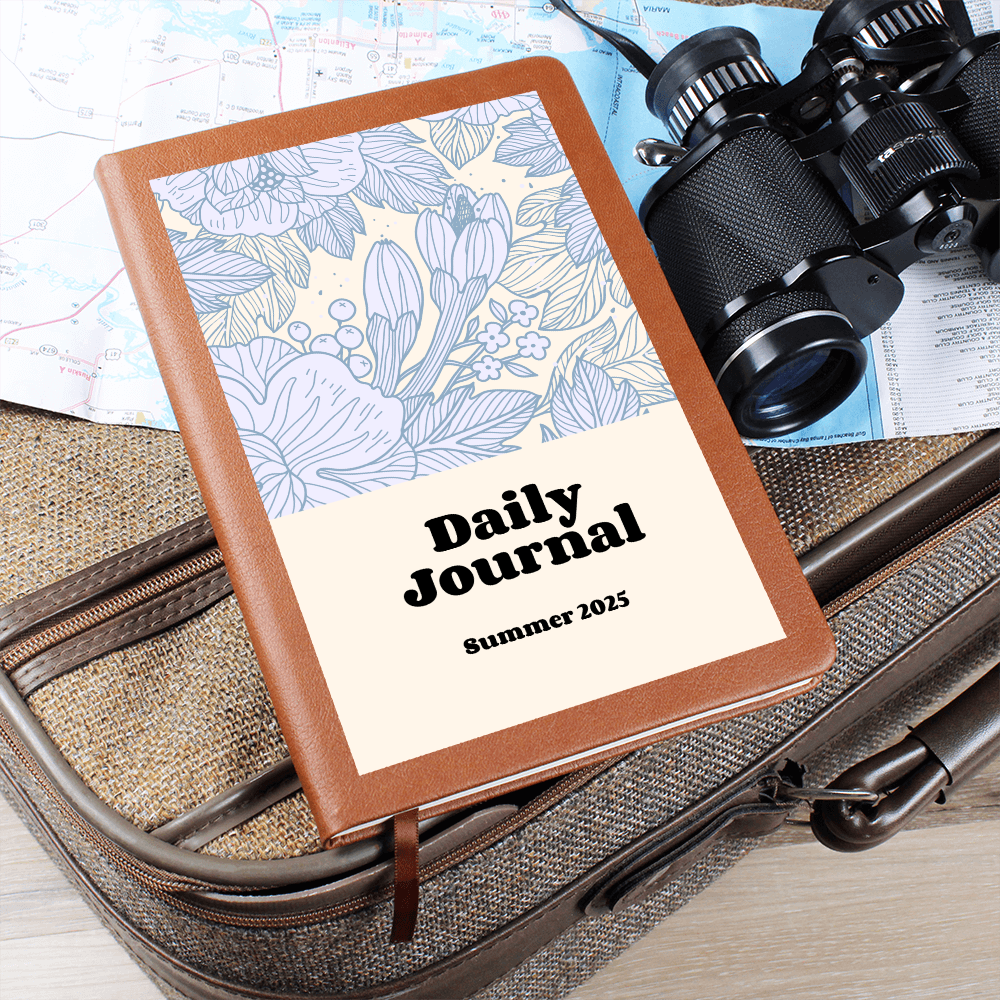 Vegan leather journal with floral design titled "Daily Journal" placed on travel items.