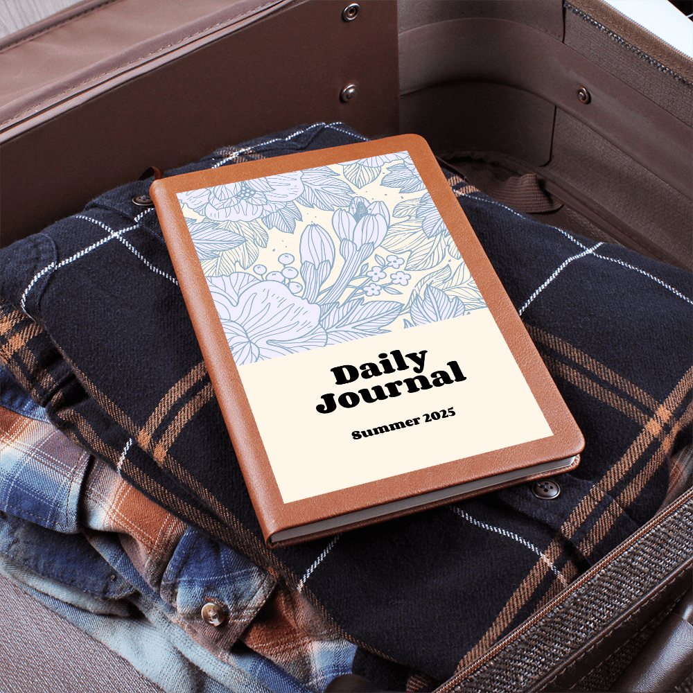 Daily Reflections journal with a floral design on a cozy plaid garment in a suitcase.