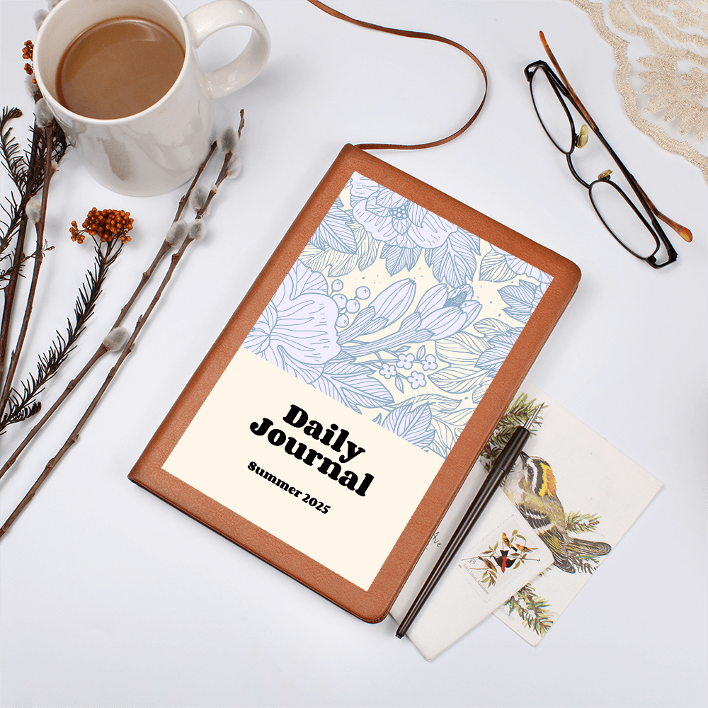 Daily Reflections journal with vegan leather cover and floral design, beside coffee and glasses.