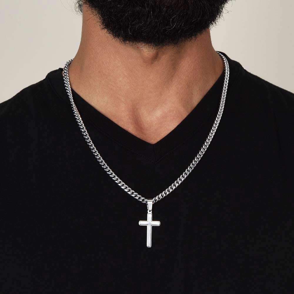 Artisan cross necklace on Cuban link chain worn around neck.