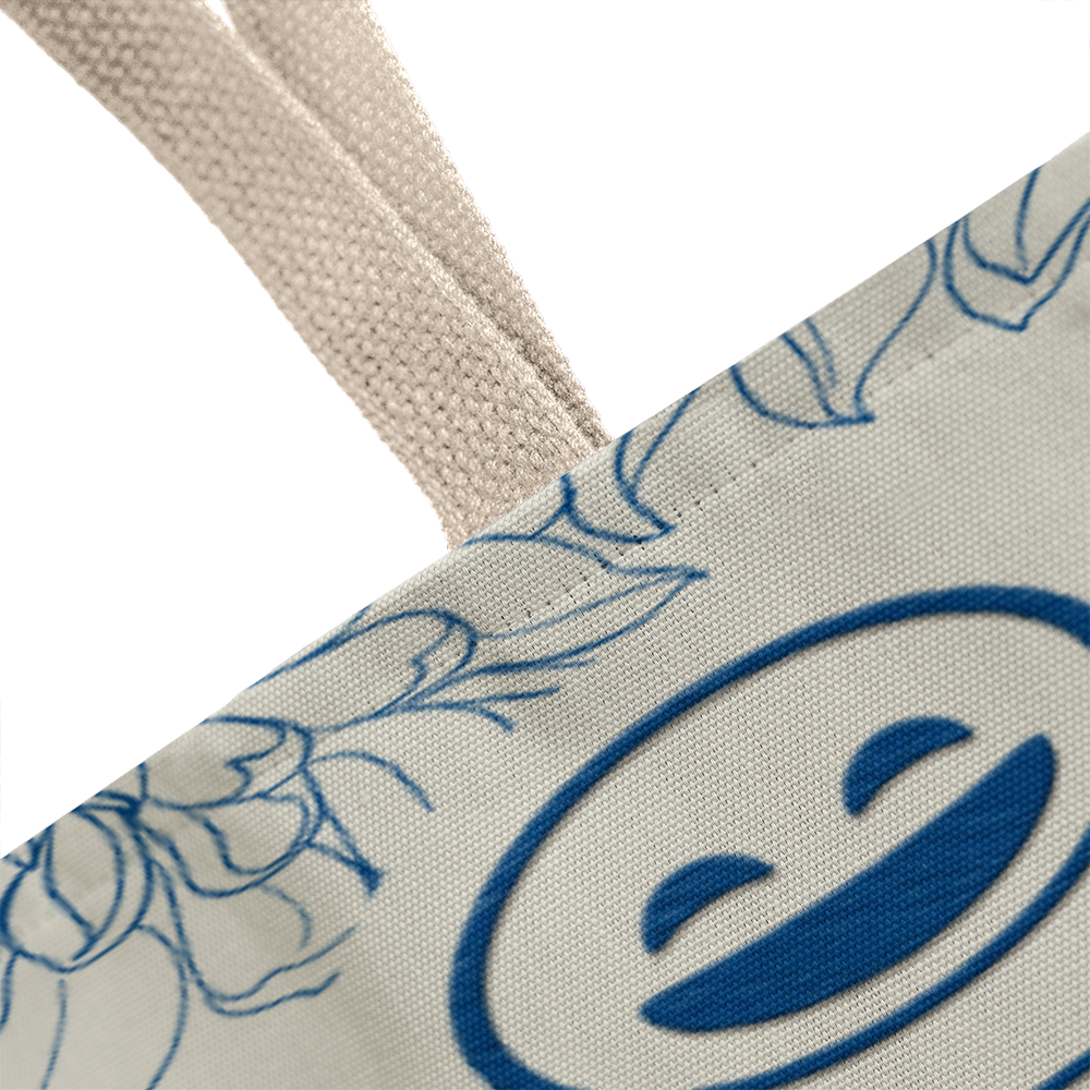 Classic tote bag with smiley design featuring blue floral accents and sturdy cotton straps.