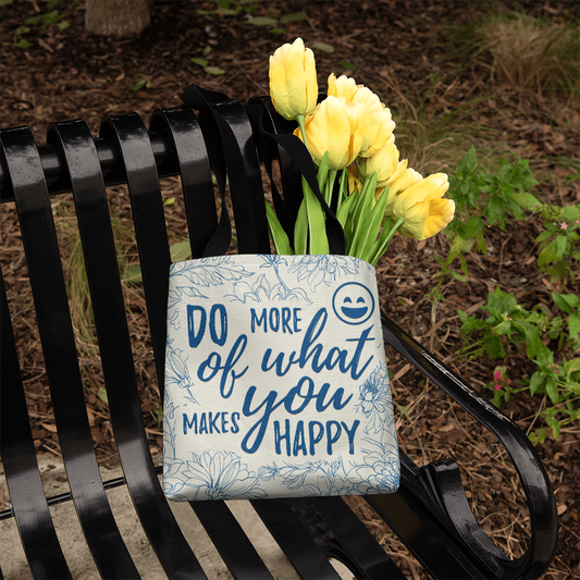 Classic tote bag with "Do More of What Makes You Happy" design, featuring yellow tulips, on a bench.