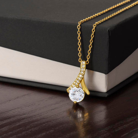 Elegant alluring necklace with gold finish and cubic zirconia pendant on gift box.