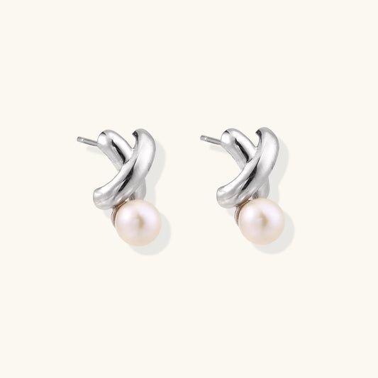 Rhodium-plated silver earrings with twisted X design and freshwater pearl drops on beige background