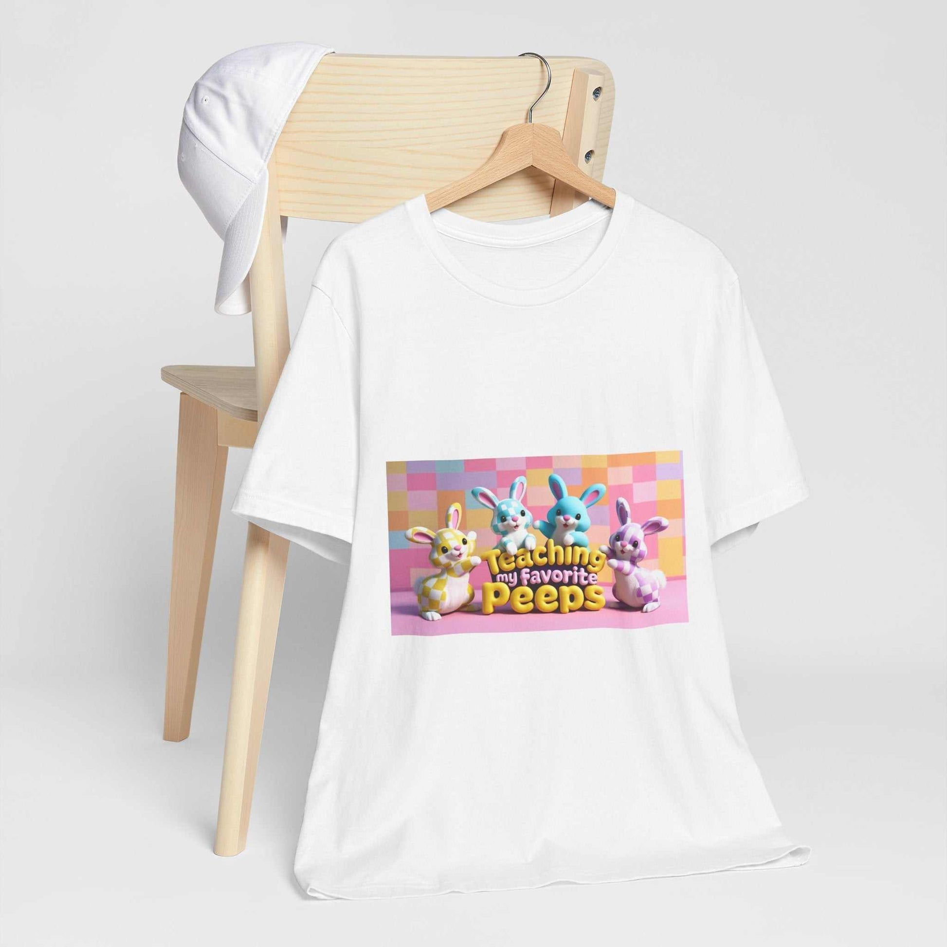Unisex jersey short sleeve tee with printed design, hanging on a wooden chair.