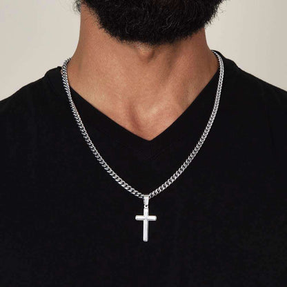 Artisan cross necklace on Cuban link chain worn around neck.